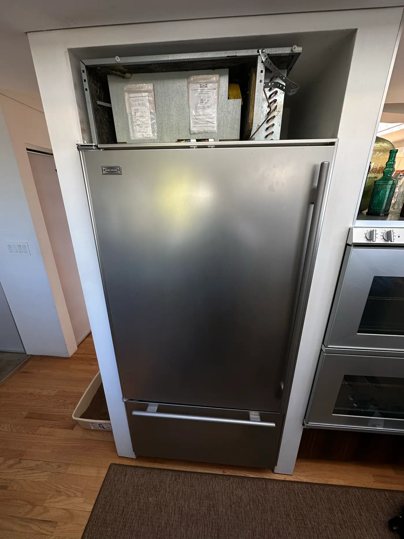 Built-in Sub-Zero refrigerator with top grille removed exposing the compressor compartment for repair