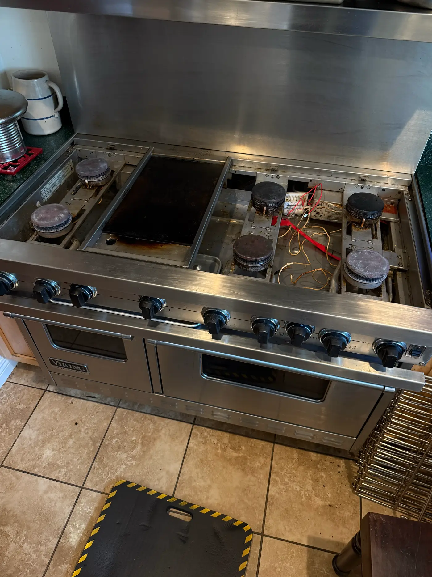 Viking 60-inch range mid-repair with grates and burner caps removed and cooktop components exposed