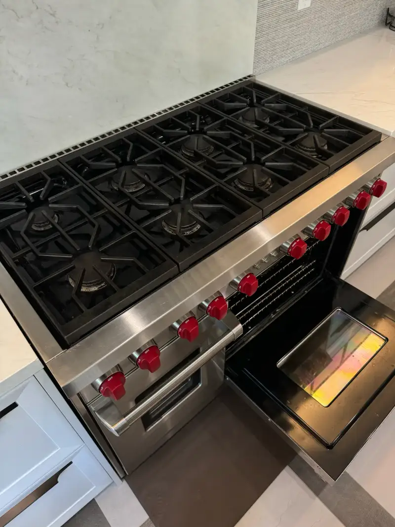 Wolf 48-inch eight-burner gas range with red knobs and open oven door in a bright white kitchen