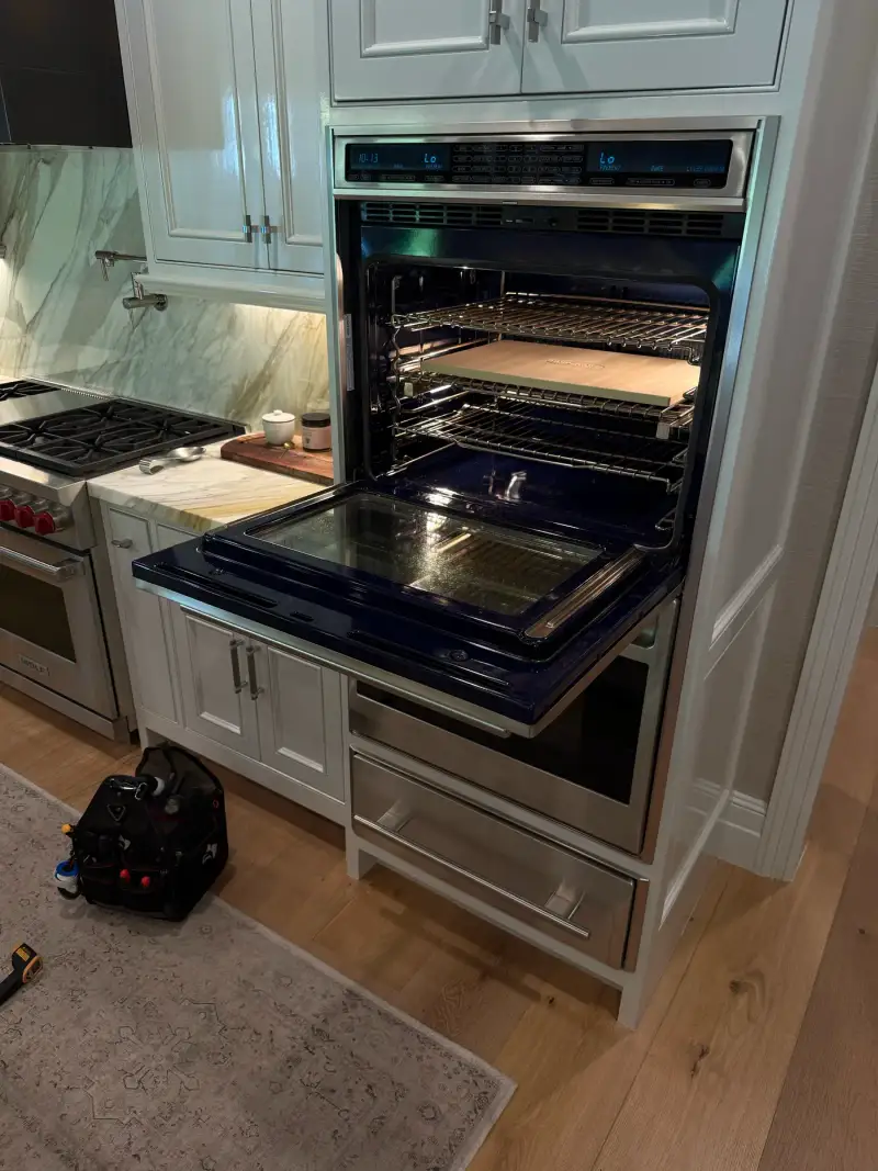 Wolf double wall oven with signature blue interior open during a service visit, tool bag on the kitchen floor